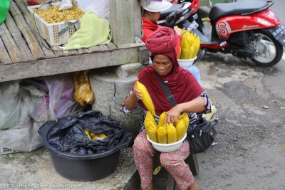 Woman selling corn beside a local fruit, vegetable and clothing market in Bali, Indonesia
