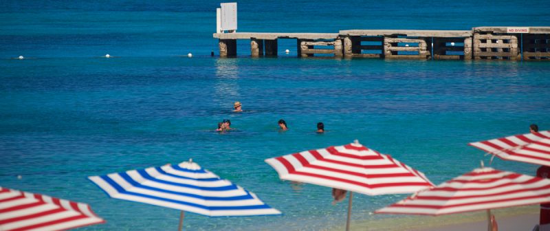 Beach umbrellas, people swimming, and a sailboat at Doctor's Cove Beach, Montego Bay, Jamaica